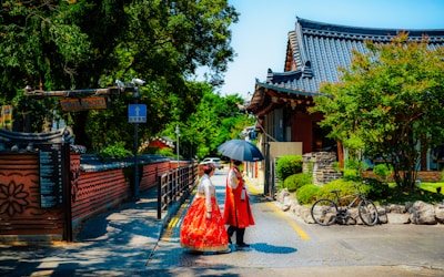 Visitor wearing traditional Korean hanbok in red and yellow standing in front of traditional palace architecture with ornate roof design typical of Korean royal compounds